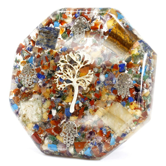 A clear resin pyramid contains colorful stones and metal shavings. A metallic tree and hamsa hand charms decorate the interior. The object sits on a plain white background.