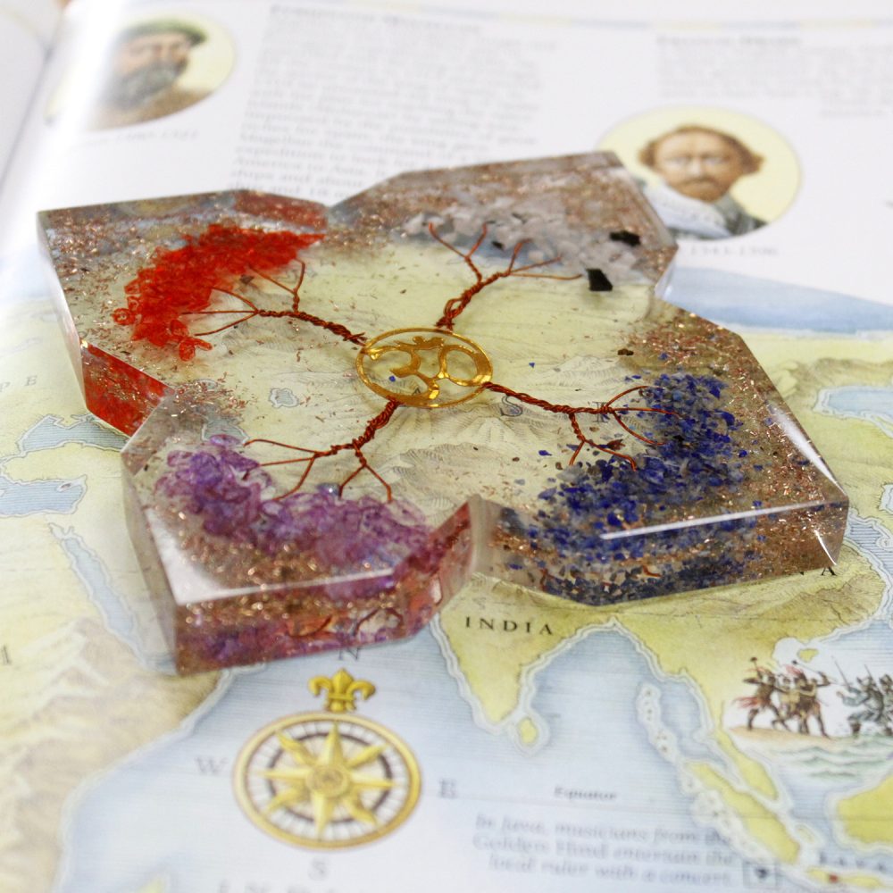A clear resin block featuring red, purple, and blue stone chips with a copper wire "tree" and Om symbol sits on a map page with the word "INDIA."