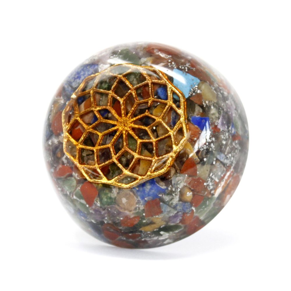An orb of resin and small colored stones sits on a white surface. A golden flower of life symbol rests on the top of the orb.