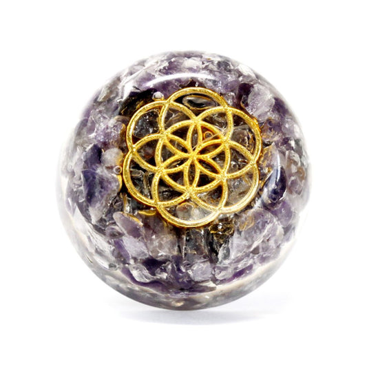 A crystal sphere displays a golden "flower of life" symbol. Embedded within the clear resin are crushed amethyst stones, set against a stark white background.