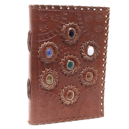 A leather-bound journal displays seven colorful gemstones, each encircled by a spiraling, textured leather accent, set on a tooled floral patterned background.