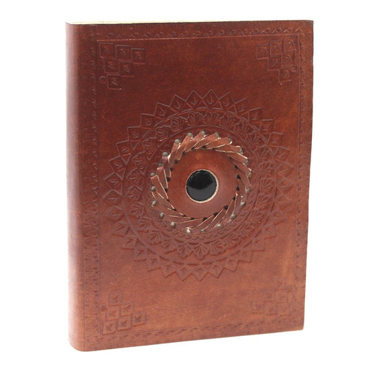 A leather-bound journal sits upright, showcasing a tooled design of concentric circles with a woven center around a dark round opening, set against a stark white background.