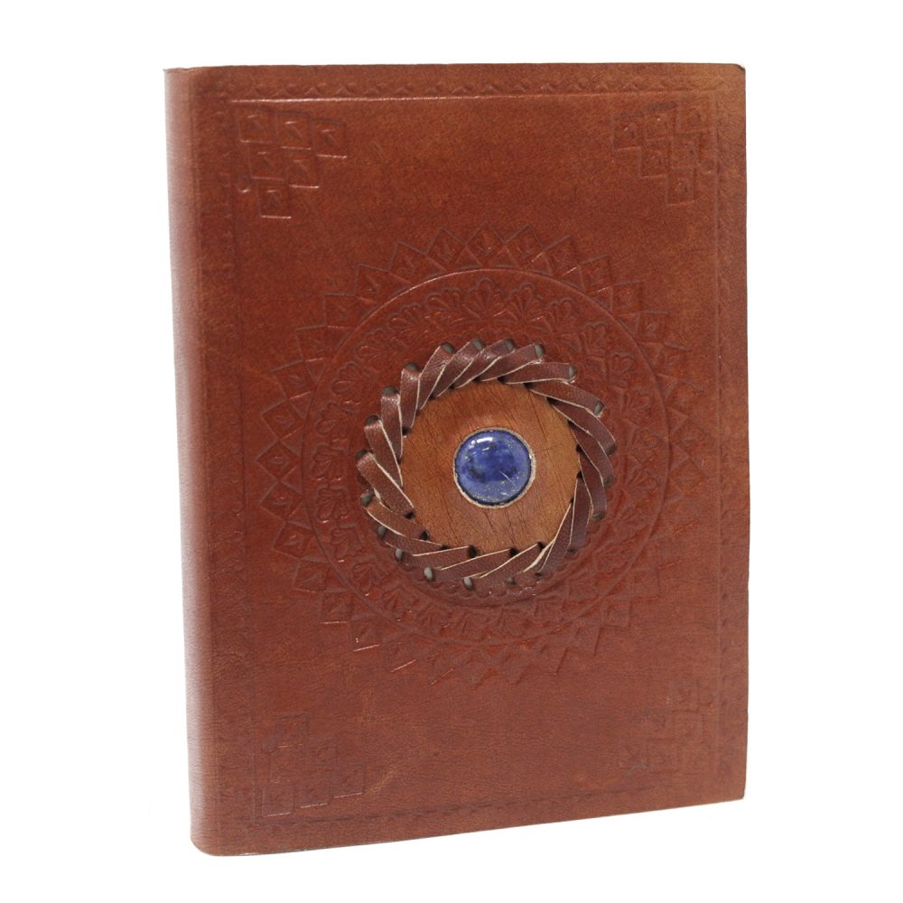 A brown leather journal with a central circular design is seen. This design features a blue stone surrounded by leather and an embossed geometric pattern on the cover.