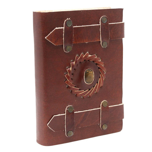The brown leather journal is clasped by two horizontal leather straps, and has a circular woven leather design with a stone in the center on the front cover.