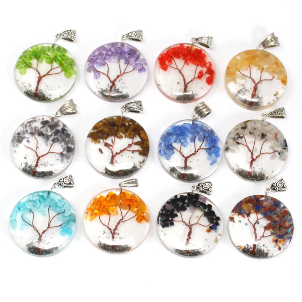 Twelve circular pendants show tree silhouettes with colorful gemstone "leaves" against a clear background, attached to silver bails on a bright white surface.