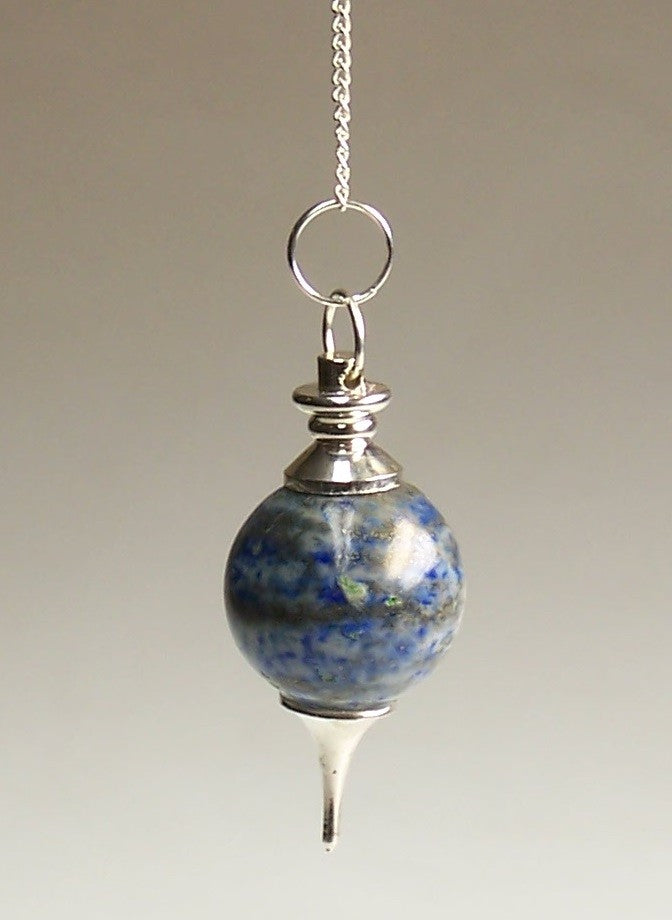 A blue orb pendulum with silver accents and a pointed end hangs from a silver chain against a soft, neutral background.