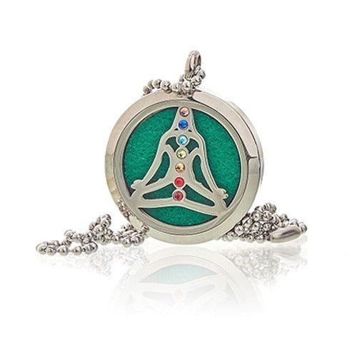 A round silver necklace pendant with a silver outline of a person meditating with different-colored chakra points lays against a white background.