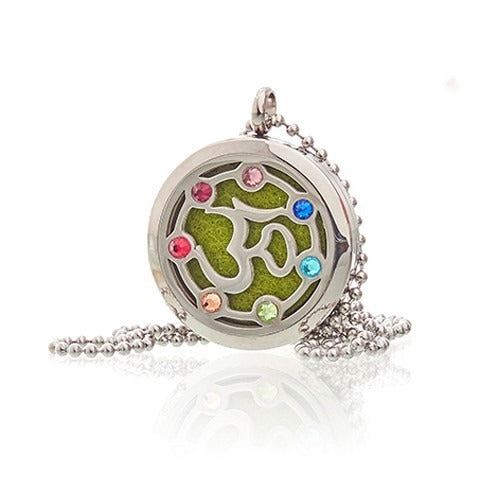 A silver chain necklace has a circular pendant, inlaid with a green felt pad shaped with the Om symbol, and is decorated with several small, colorful gemstones, and lays on a white surface.