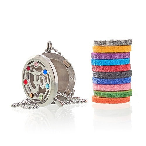 An open silver locket with an Om symbol, outlined by colorful gems, sits next to a stack of colorful felt circles on a white background.