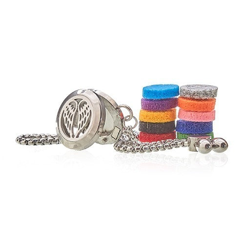 A silver necklace locket, with angel wing cutouts, rests near stacks of colorful felt circles in a white space, likely for displaying jewelry.