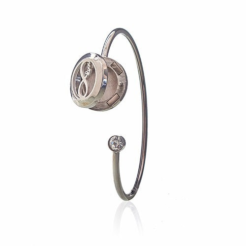 A polished silver bangle displays an infinity symbol enclosed in a circular locket. The bangle is open and ends with a small clear crystal.