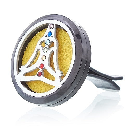 The gray car vent clip contains a yellow absorbent pad, overlaid with a silver cut-out of a figure in lotus position with seven colored gemstones along the body.