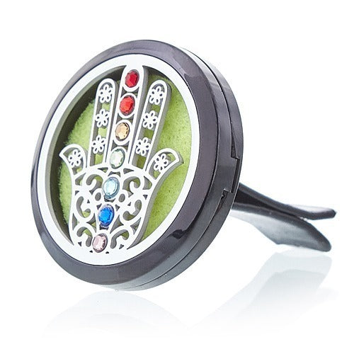 A decorative black car vent clip features a filigree hand design with colorful gemstone accents on a lime green background.