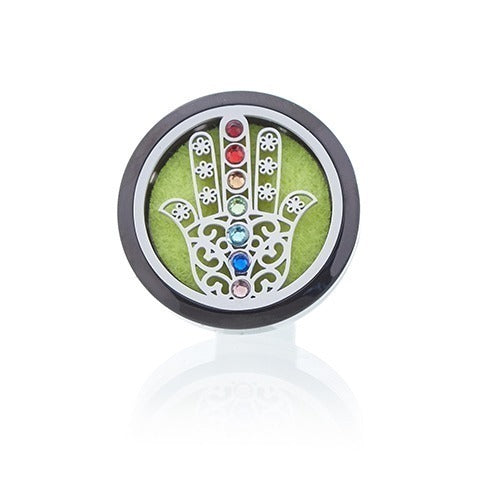 The black-rimmed, round car air freshener displays a filigreed Hamsa hand over a green pad, with colorful gemstone accents. It's shown against a plain white background with a reflection.