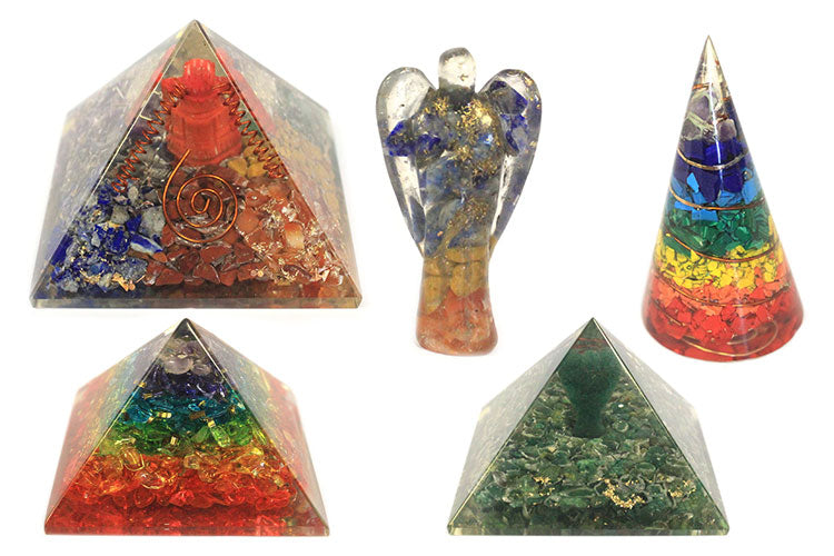 Several orgonite items rest on a white surface: Two pyramids, a cone, and an angel figurine, all constructed of colorful crystals in epoxy.