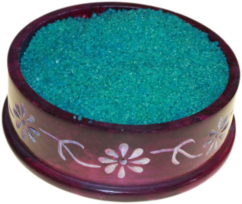 Teal granular material sits in a round, purple, carved stone bowl adorned with floral designs.