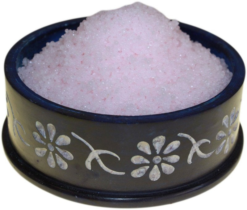 Pink bath salts rest in a dark blue, flower-decorated bowl.