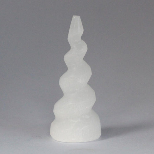 A translucent, off-white, crystal sculpture spirals upward from a widened base, tapering to a point in the center of a neutral, light gray backdrop.