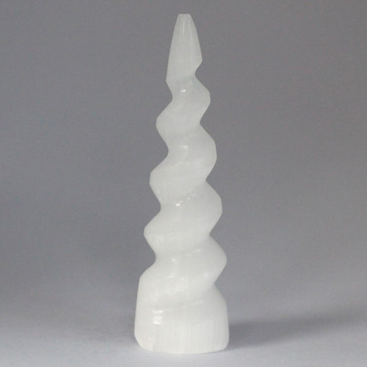 A white, spiral, slightly translucent tower tapers to a point, sitting still against a light grey, neutral background.