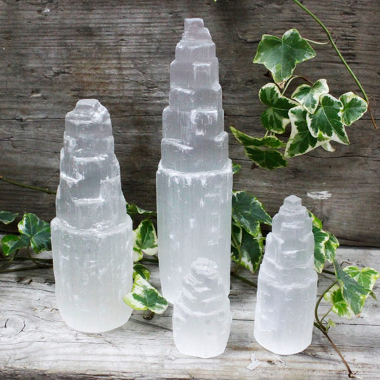 Three selenite towers stand upright among ivy on a weathered wooden surface. The towers are different sizes and have a stepped, pagoda-like shape.