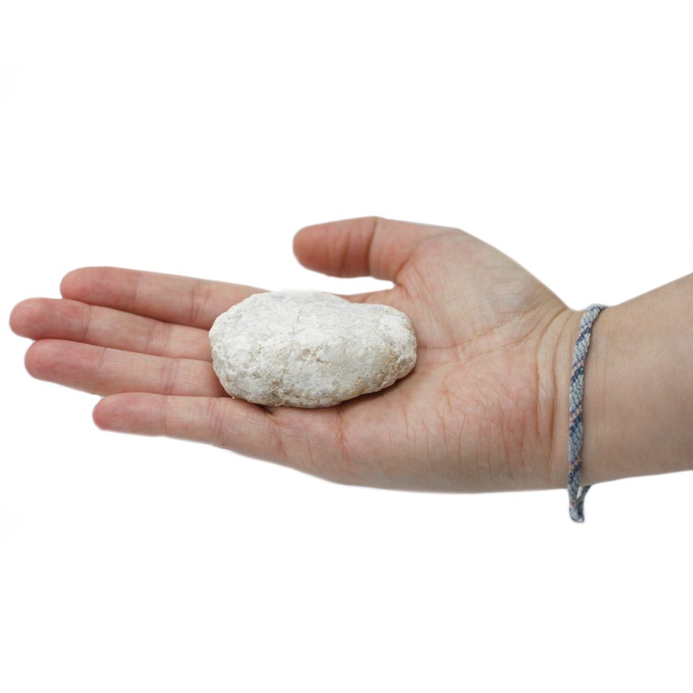 A roughly oval, white stone rests in the open palm of a hand, which is adorned with a knotted bracelet. The background is white.