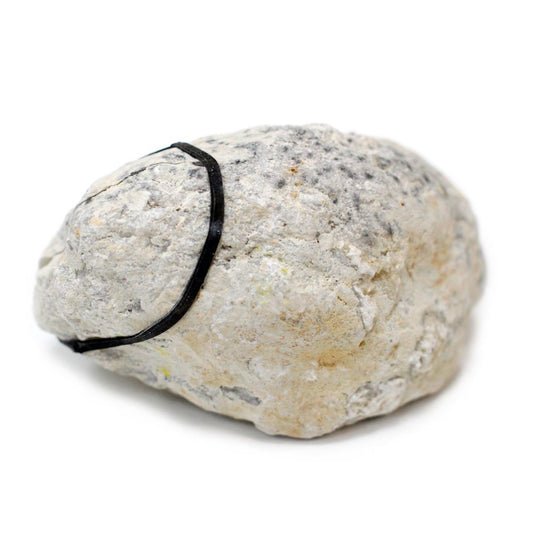 A small, textured, grey and beige rock has a thin black rubber band wrapped around it, sitting on a plain white surface.