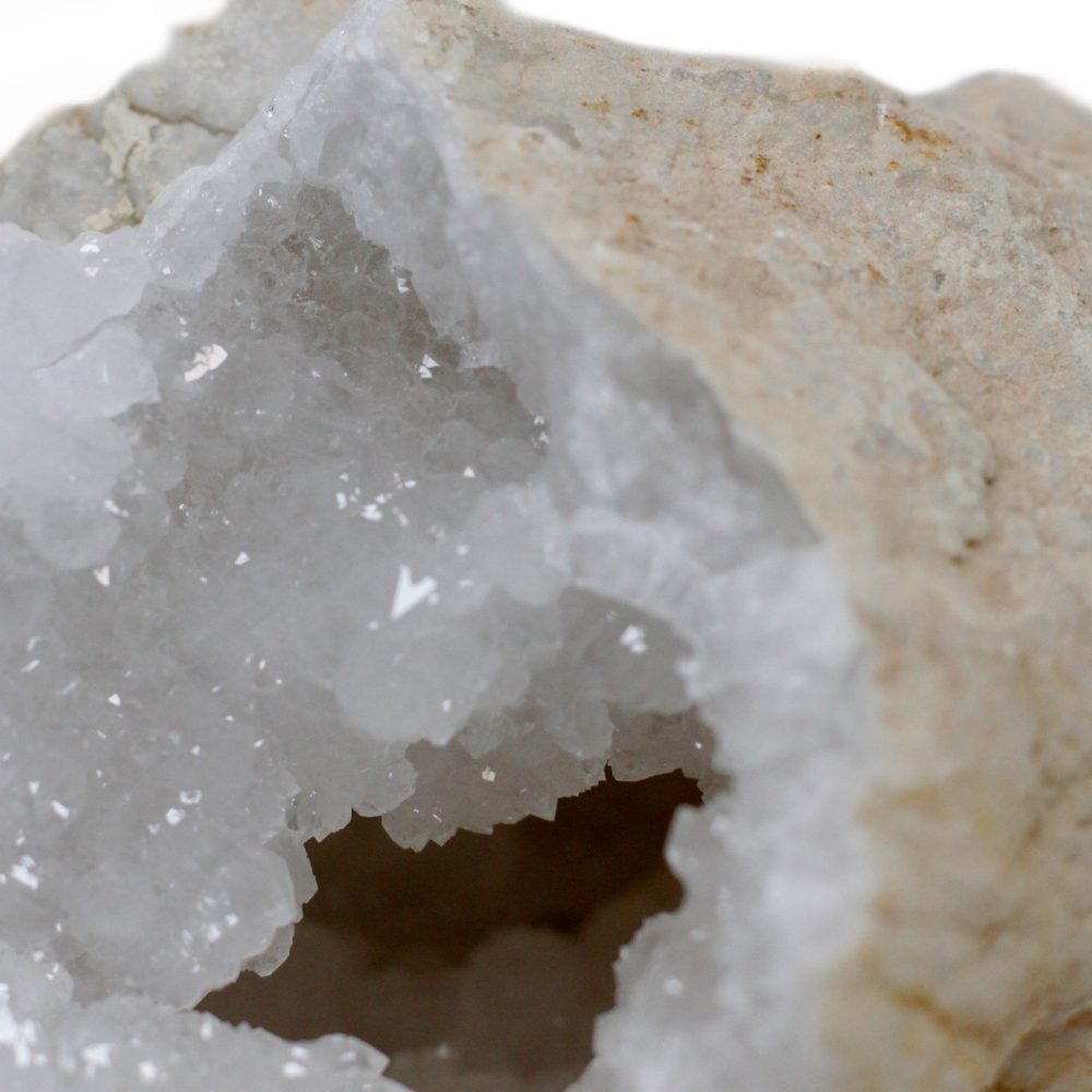 A geode sits, its outer tan shell cracked open, revealing a sparkling, white crystalline interior.
