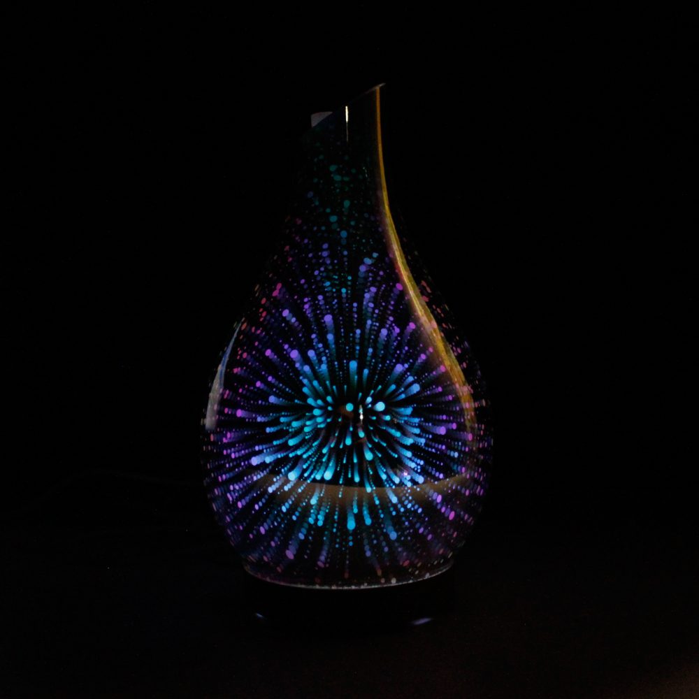 A teardrop-shaped diffuser glows with radiating, colorful lights. The surrounding environment is black, making the object's colors appear brighter.