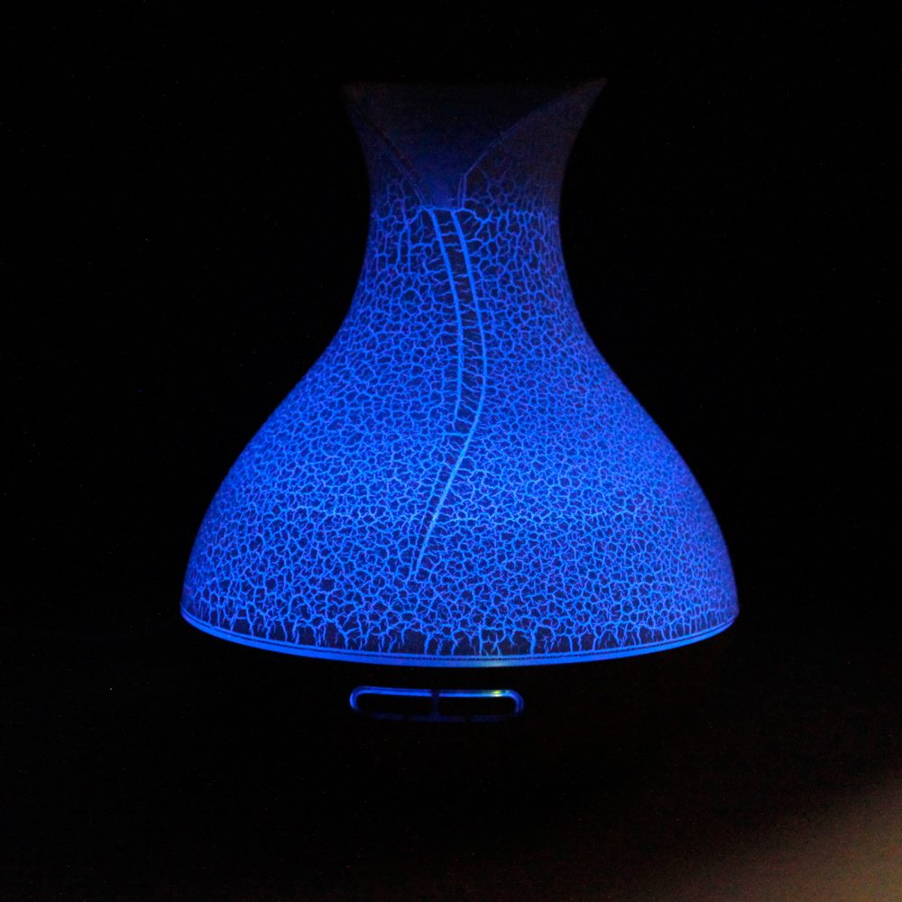 Vase-shaped diffuser emits blue light with a cracked pattern, casting a glow against the dark background.