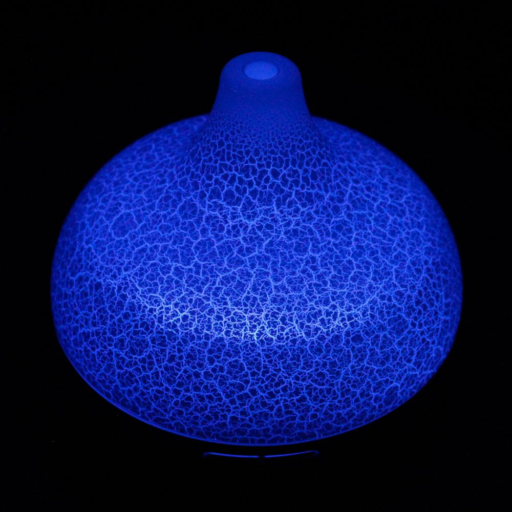 A glowing, globular diffuser sits in darkness. The textured surface radiates bright blue light, reminiscent of a lightning bolt pattern.