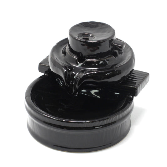 Black ceramic teapot with a round base and a lid, sitting on a circular tray. The teapot features a small spout and handle, all within a plain white backdrop.
