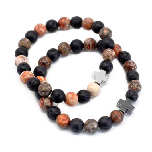 Two bracelets made of spherical beads, black lava stone and mottled shades of brown, rest on a white background. Each features a metallic cross.