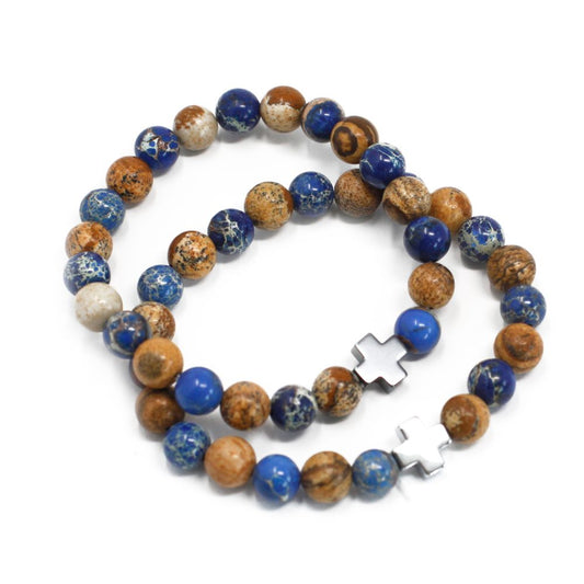 Two beaded bracelets, with blue and brown stones and silver cross charms, lay coiled on a plain white background.