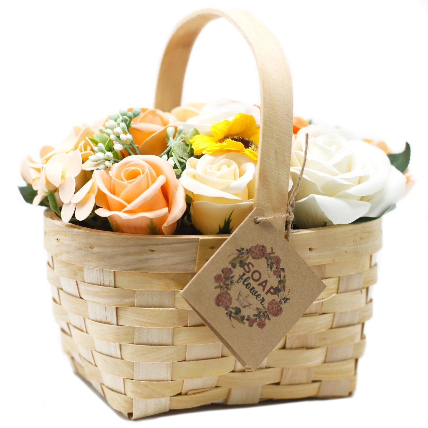A light-wood woven basket holds assorted peach, white, and yellow flowers. A cardboard tag reading “SOAP flower” in a floral wreath hangs from the handle.