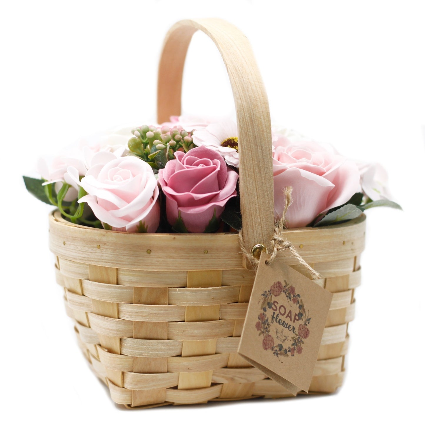 A wicker basket holds pastel roses and greenery. A brown tag reading “SOAP flower” is tied to the side. The basket is set against a white background.