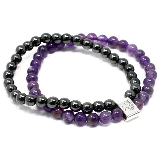 Two beaded bracelets, one purple and one black, are layered on a white surface. The purple bracelet has a square, silver charm.