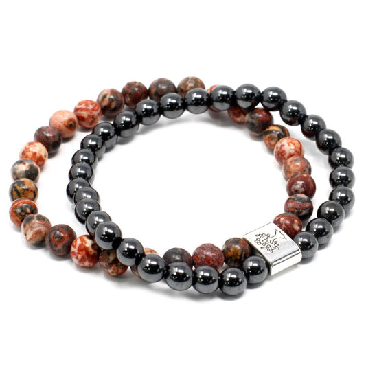 Two beaded bracelets circle each other on a white surface. One is made of brown, tan, and red spotted beads, and the other is made of metallic black beads with a silver charm.