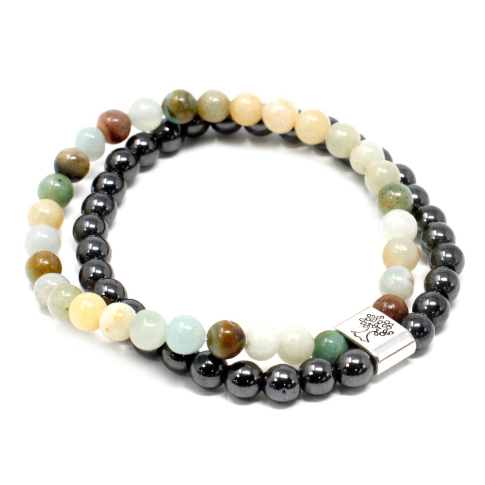 Two beaded bracelets, one with multi-colored stone beads, the other with metallic black beads, are coiled on a white surface. A silver bead with a tree design connects the ends of the stone bracelet.