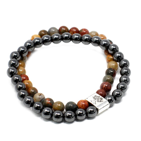 Two beaded bracelets, one with hematite beads and the other with multi-colored jasper beads, are arranged in overlapping circles. A rectangular silver clasp etched with a tree design connects the bracelets. The background is white.