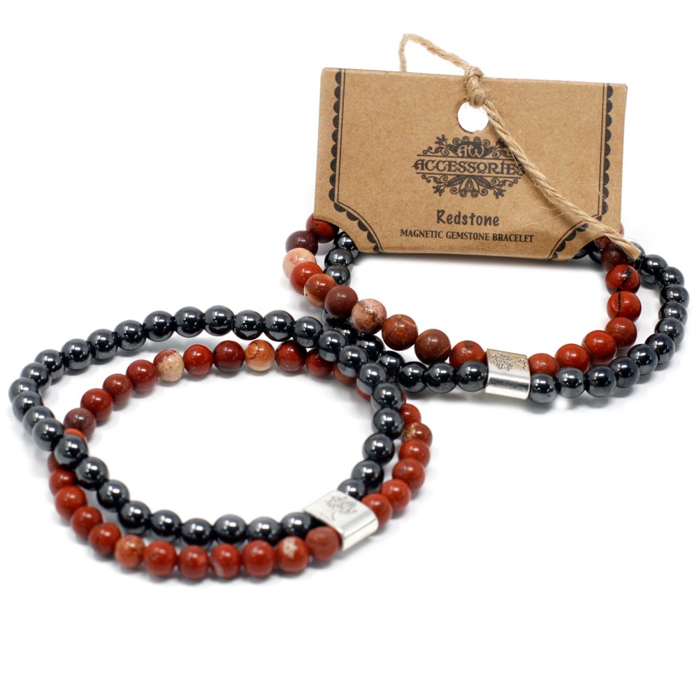 Two beaded bracelets are stacked atop a white surface. Each bracelet consists of alternating hematite and redstone beads and includes a silver accent. A brown tag with “Accessories Redstone MAGNETIC GEMSTONE BRACELET” printed on it sits behind the bracelets.
