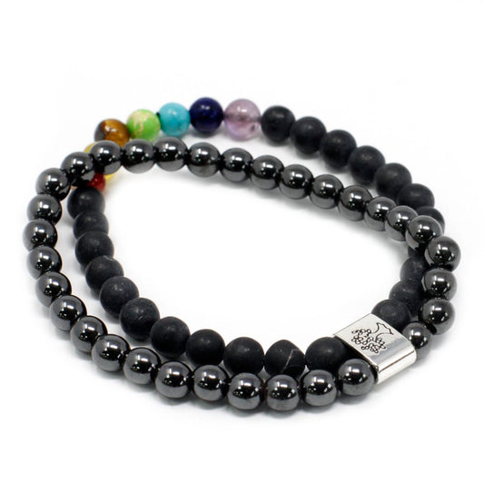 Two beaded bracelets curl inward against a white backdrop. One bracelet has seven chakra-colored beads followed by matte black beads; the second bracelet alternates hematite and matte black beads, joined by a silver charm.