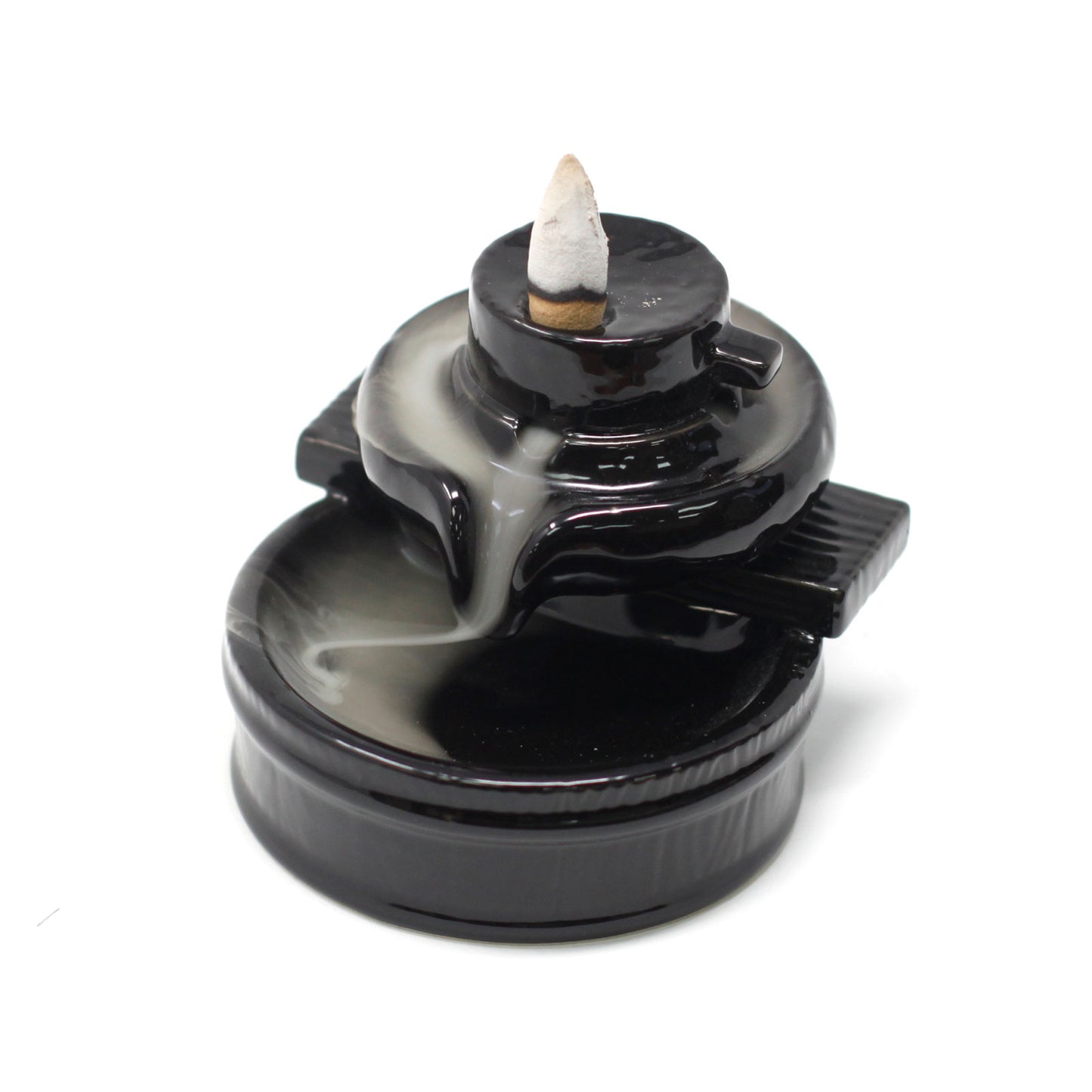 A black ceramic incense holder features a lit cone at the top. Smoke gracefully cascades down tiered surfaces, resembling a waterfall. The scene creates a calming atmosphere.