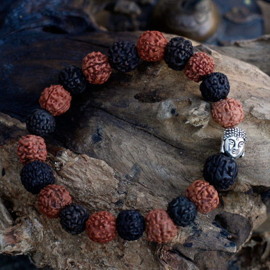 A beaded bracelet lies on weathered wood. The bracelet has alternating dark and reddish-brown, rough-textured beads, with a silver Buddha head bead.