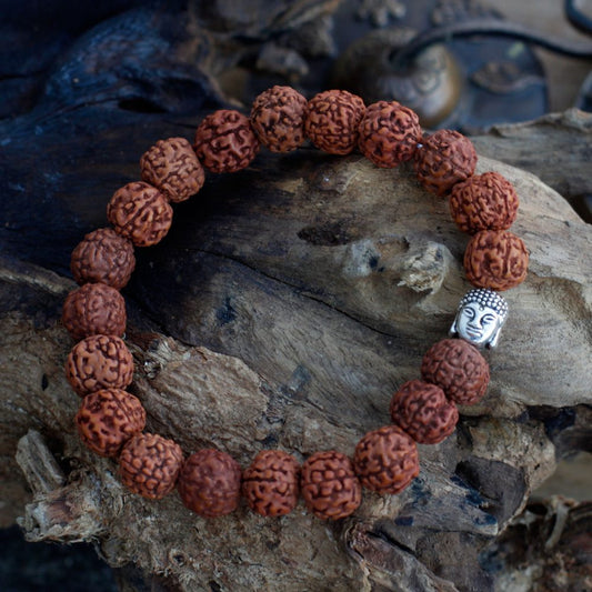 A beaded bracelet rests on weathered wood. The bracelet features brown, textured beads, and a single, silver-colored Buddha charm.