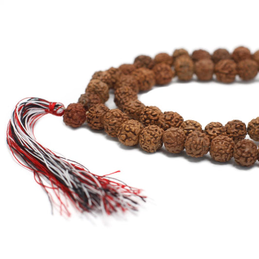 A string of textured brown beads with a tasseled end curls through a clean, white space. The tassel is made of threads of red, white, and black.