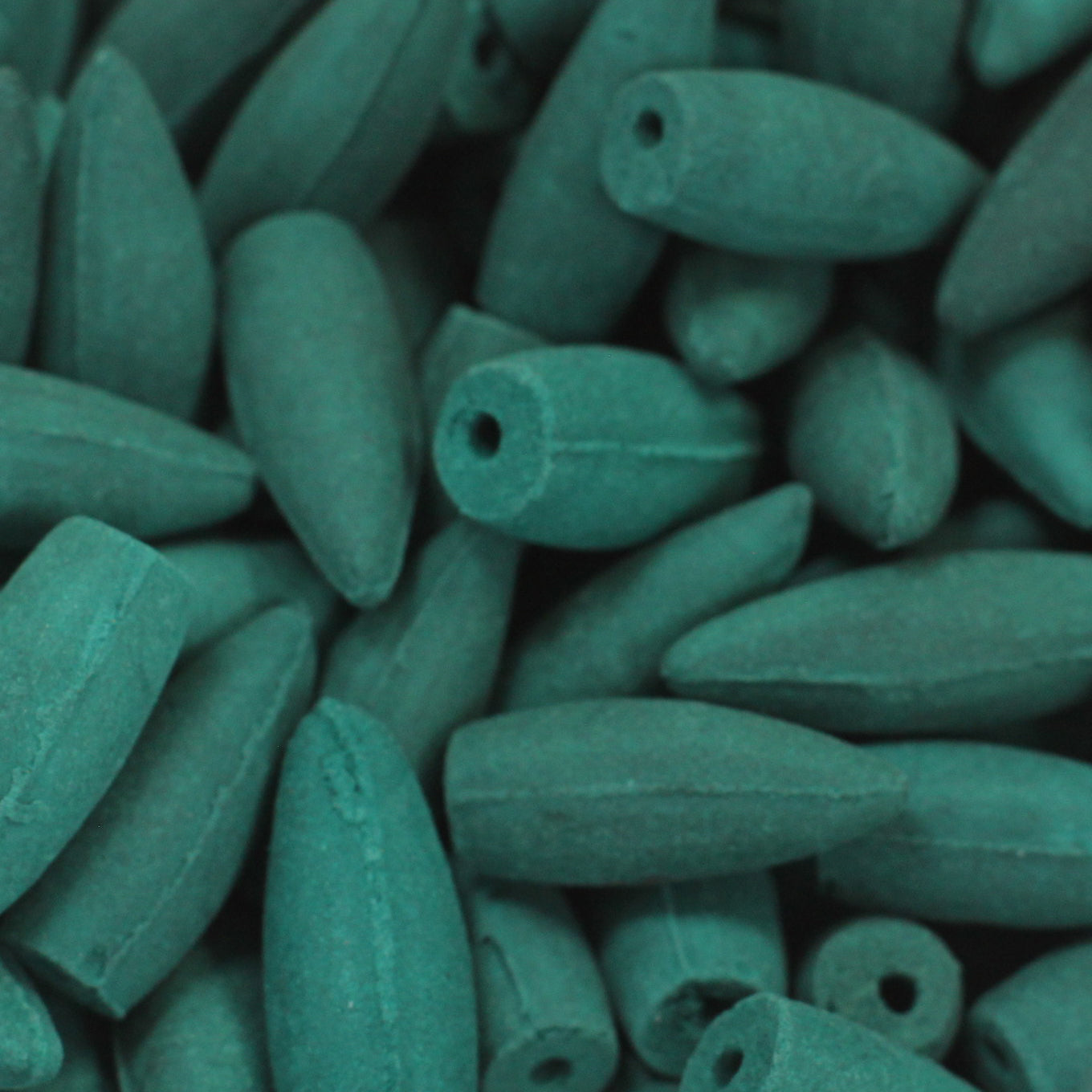 Elongated, teal-colored stones with smooth surfaces and small holes are densely clustered together, filling the entire frame.