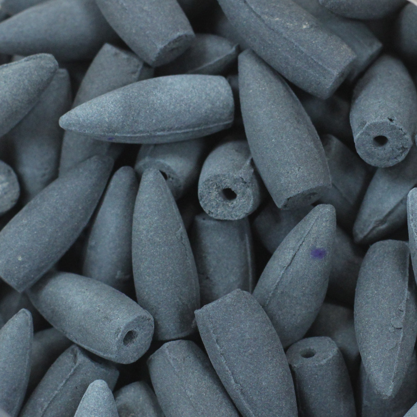 Gray, cone-shaped incense cones with a small hole at one end are tightly clustered together, creating a textured pile without any visible text present.
