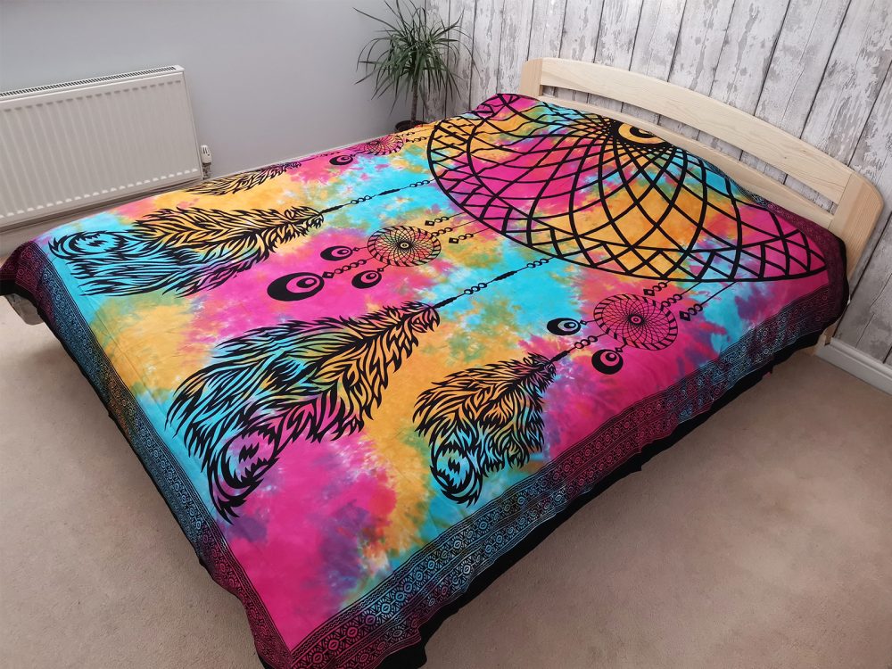 A tie-dye tapestry, featuring dreamcatchers and feathers, adorns a bed in a bedroom.