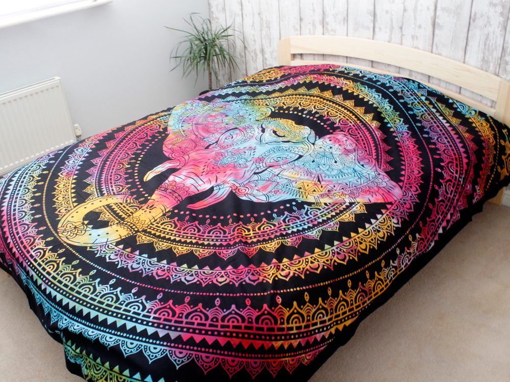 A colorful mandala tapestry, featuring a tie-dye elephant, is draped over a bed in a bedroom.