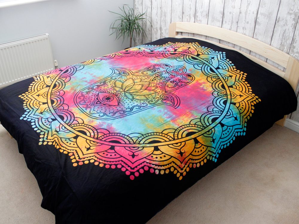 A tie-dye tapestry, featuring a Hamsa hand within a mandala design, rests on a bed in a bedroom.
